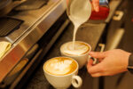 Hände bereiten zwei Cappuccinos vor